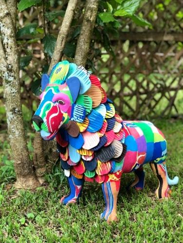 Large hand-carved multicolored lion sculpture made of upcycled flip flops by Ocean Sole set up outside in a garden.