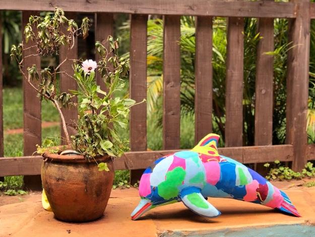 Hand-carved multicolored dolphin sculpture made of upcycled flip flops by Ocean Sole sitting on an outdoor patio.