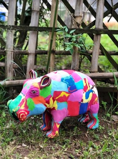 Large multicolored hippo sculpture made of upcycled flip flops by Ocean Sole sitting in a garden.