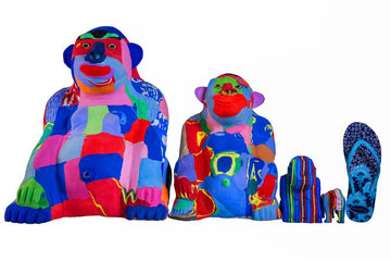 Four hand-carved multicolored sitting gorilla sculptures made of upcycled flip flops by Ocean Sole lined up in size comparison to a flip flop.