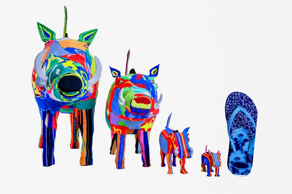 Four hand-carved multicolored warthog sculptures made of upcycled flip flops by Ocean Sole lined up in size comparison to a flip flop.