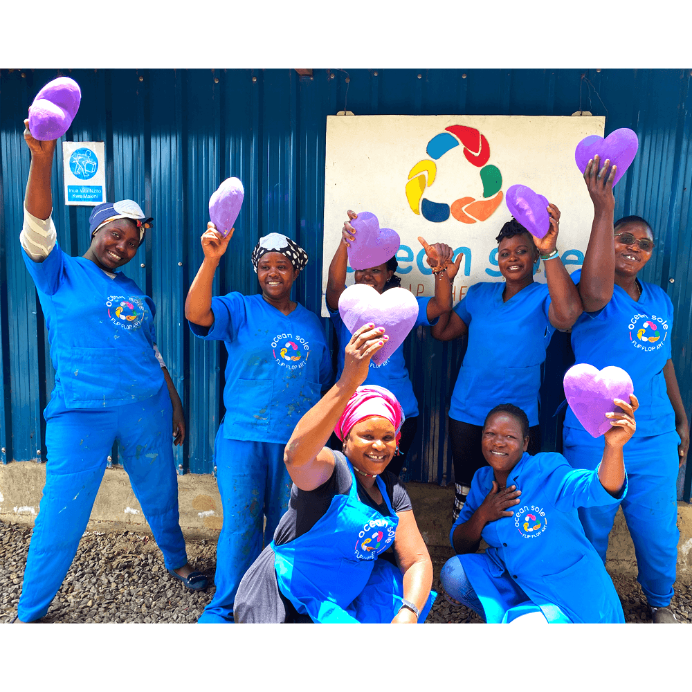 Ocean Sole artisans holding up hand-carved purple heart sculpture made of upcycled flip flops by Ocean Sole in honor of International Women's Day.