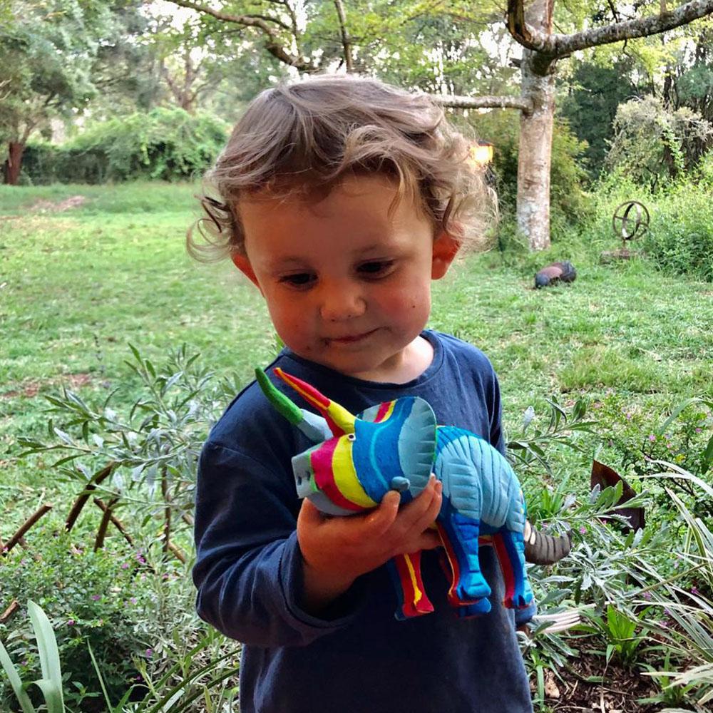 Young boy playing with a hand-carved multicolored triceratops sculpture made of upcycled flip flops by Ocean Sole.
