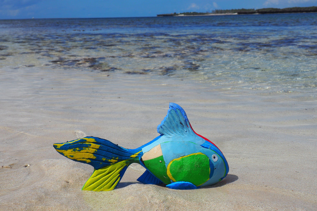 Hand-carved multicolored reef fish sculpture made of upcycled flip flops by Ocean Sole sitting on the beach.