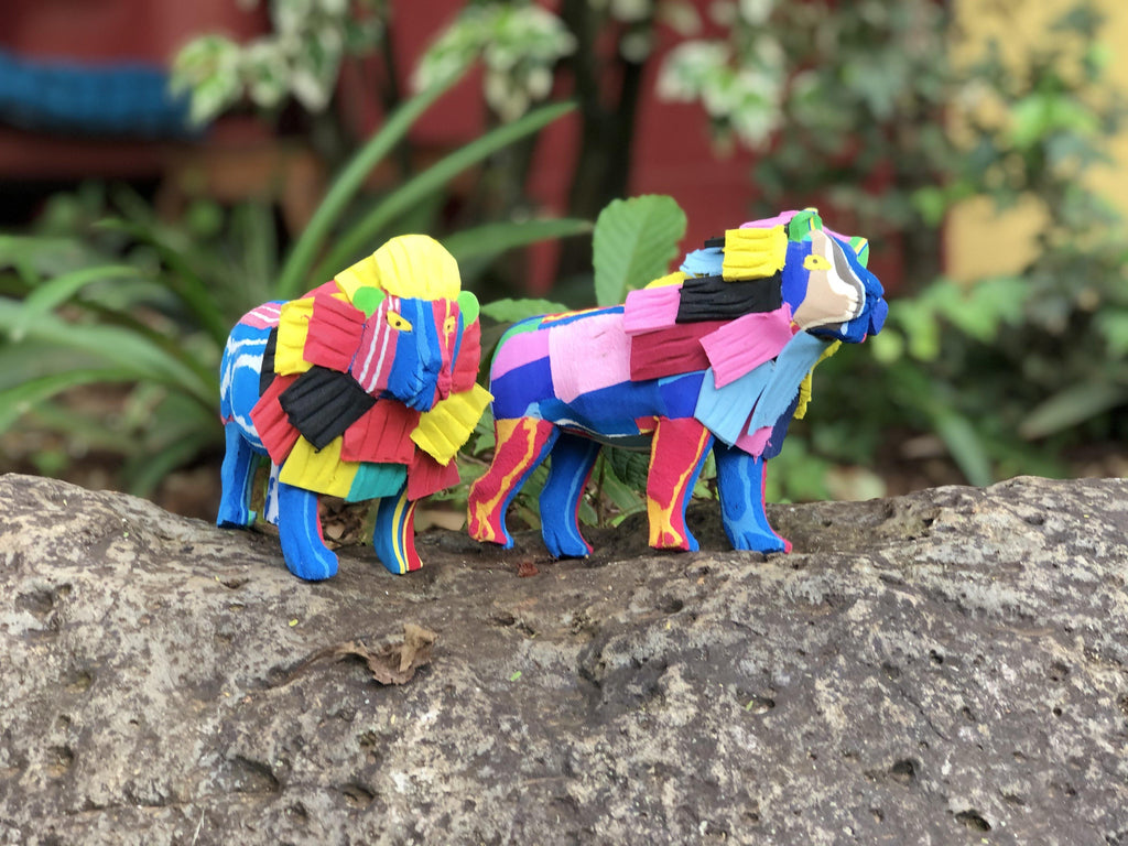 Two hand-carved multicolored standing lion sculpture made of upcycled flip flops by Ocean Sole sitting outside in a garden.