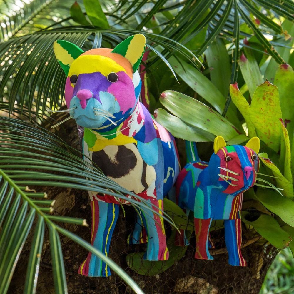 Hand-carved multicolored standing cat sculpture made of upcycled flip flops by Ocean Sole standing in greenery.