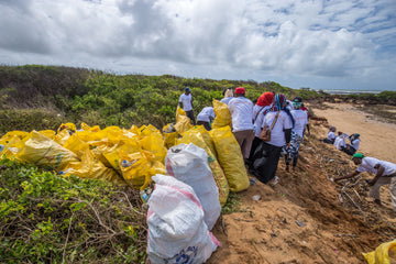 Ocean Sole team surrounded by dozens of bags of collected beach trash after cleaning up Kenyan Beaches on International Beach Cleanup Day.
