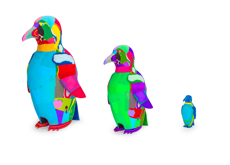 Three hand-carved multicolored penguin sculptures made of upcycled flip flops by Ocean Sole lined up in size comparison.