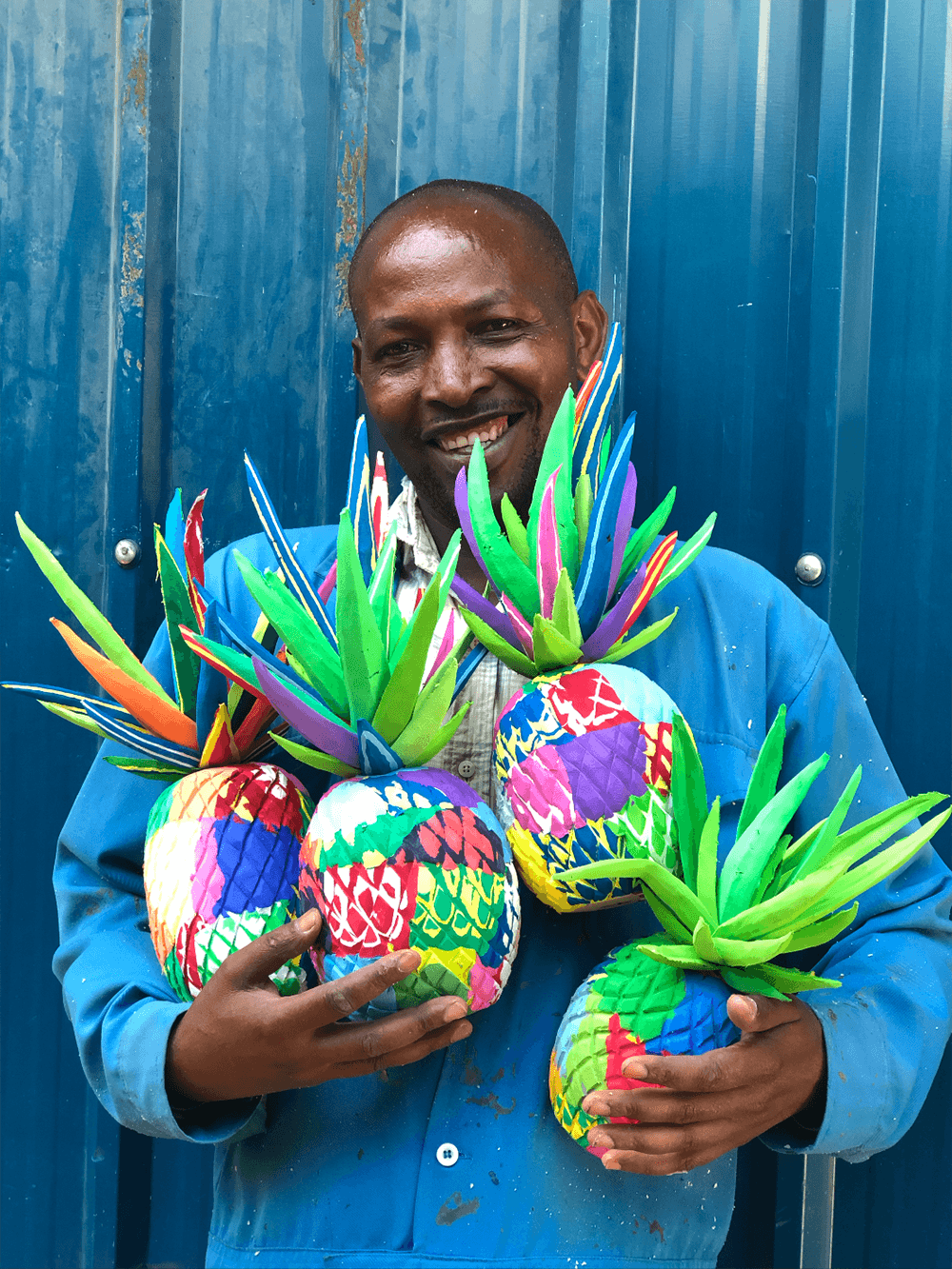 Bunch of hand-carved multicolored pineapple sculpture made of upcycled flip flops in the arms of an Ocean Sole artisan.