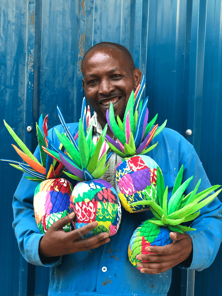 Bunch of hand-carved multicolored pineapple sculpture made of upcycled flip flops in the arms of an Ocean Sole artisan.