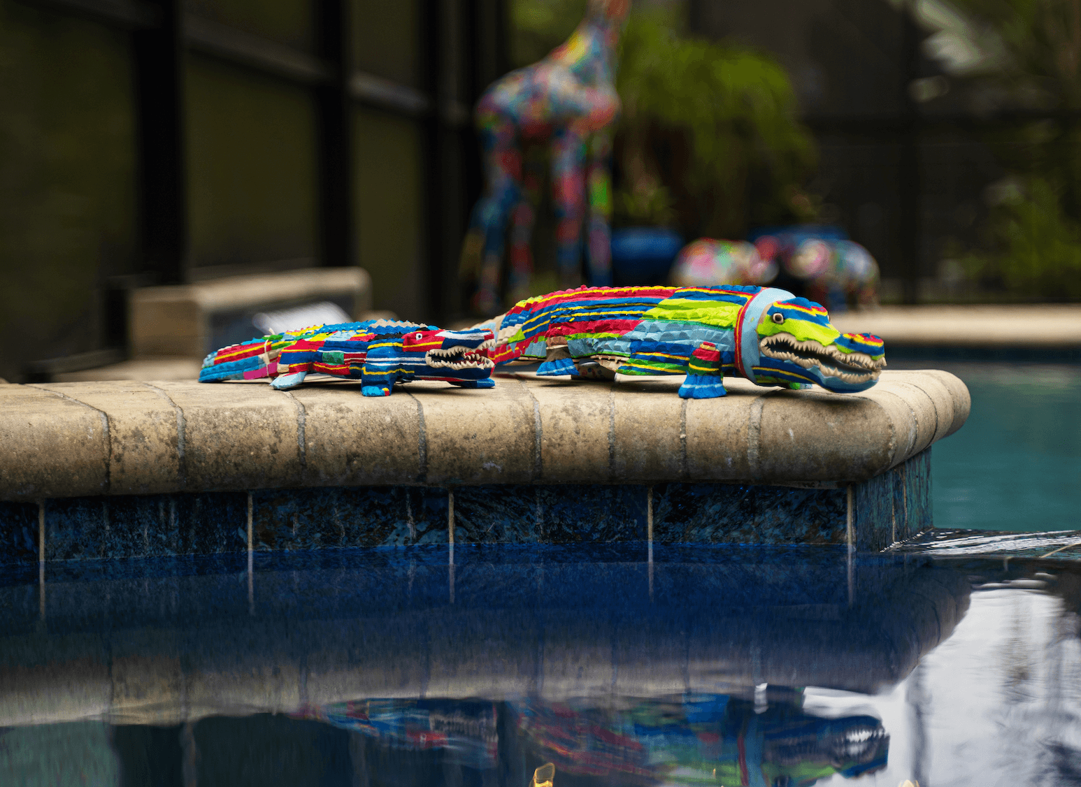 Multicolored alligator sculpture made of upcycled flip flops by Ocean Sole sitting on edge of pool.