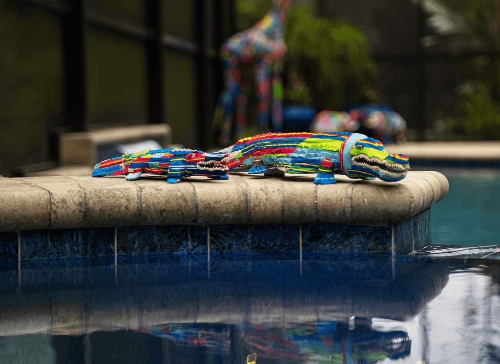 Multicolored alligator sculpture made of upcycled flip flops by Ocean Sole sitting on edge of pool.