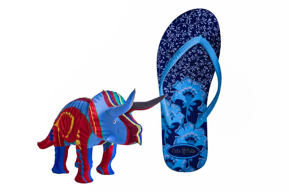 Hand-carved multicolored triceratops sculpture made of upcycled flip flops by Ocean Sole in size comparison to a flip flop. 