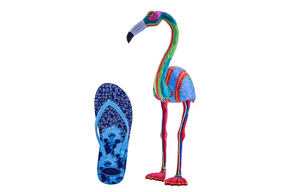 Hand-carved multicolored flamingo sculpture made of upcycled flip flops by Ocean Sole in size comparison to a flip flop.