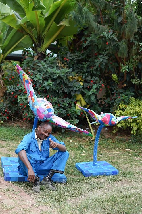 Mounted manta ray sculptures made of upcycled flip flops by Ocean Sole sitting next to a Ocean Sole artisan.