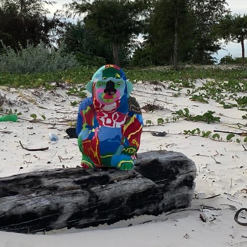Hand-carved multicolored sitting gorilla sculpture made of upcycled flip flops by Ocean Sole sitting on the beach.