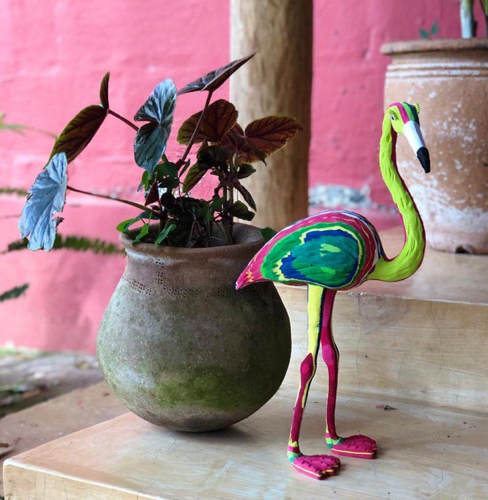 Hand-carved multicolored flamingo sculpture made of upcycled flip flops by Ocean Sole standing next to a potted plant.